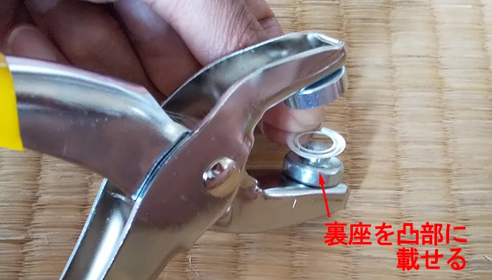 ハトメパンチの使い方とハトメの付け方解説1：裏座を凸部に載せる様子を撮影した写真に解説コメントを入れた写真画像
※Original image actually taken by myself：Copyright © とある建築士の憂鬱 All Rights Reserved.